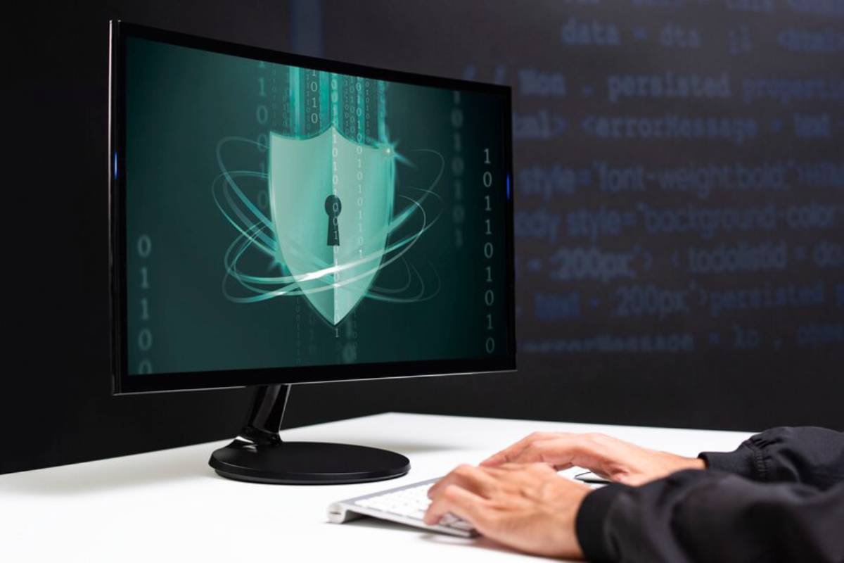 A person typing on a keyboard with a computer screen displaying a digital shield and key symbol, representing cybersecurity concepts.