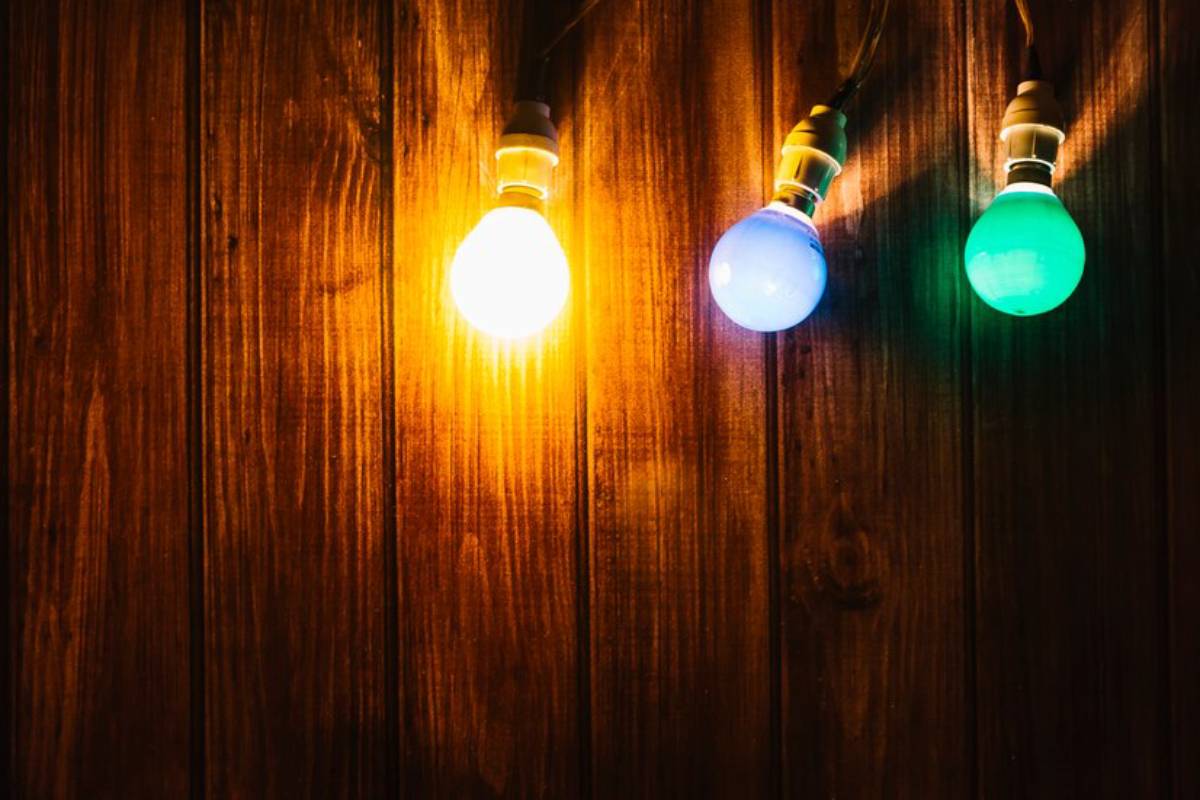 Three colorful light bulbs—orange, blue, and green—illuminated against a rustic wooden background.